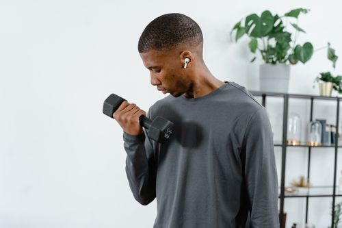 Free Man working out with dumbbell indoors, wearing wireless earbuds, showcasing a healthy lifestyle. Stock Photo