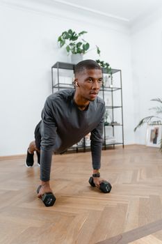 A young man performs push-ups with dumbbells in a home setting, focusing on fitness.