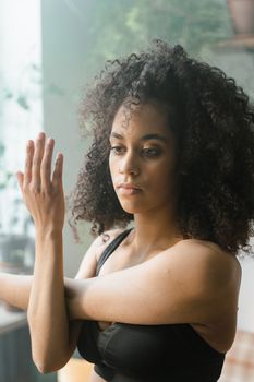 Young woman in black sports bra stretching indoors with natural lighting.
