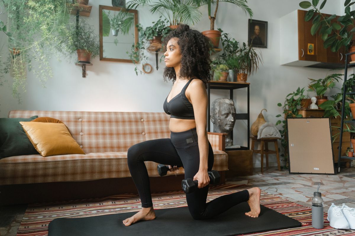 Woman exercising with dumbbells and a training mat at home