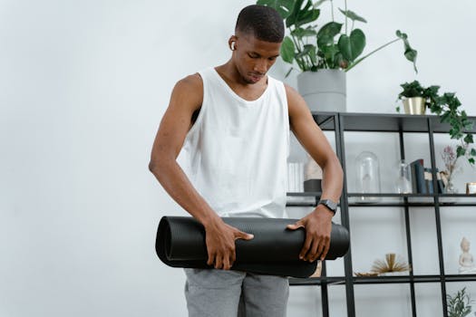 A man prepares for a yoga session by rolling up his yoga mat indoors.