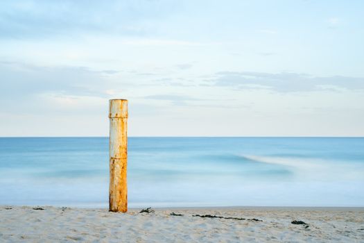 Calm ocean scene in Sydney with a lone weathered post standing on the sandy shore.