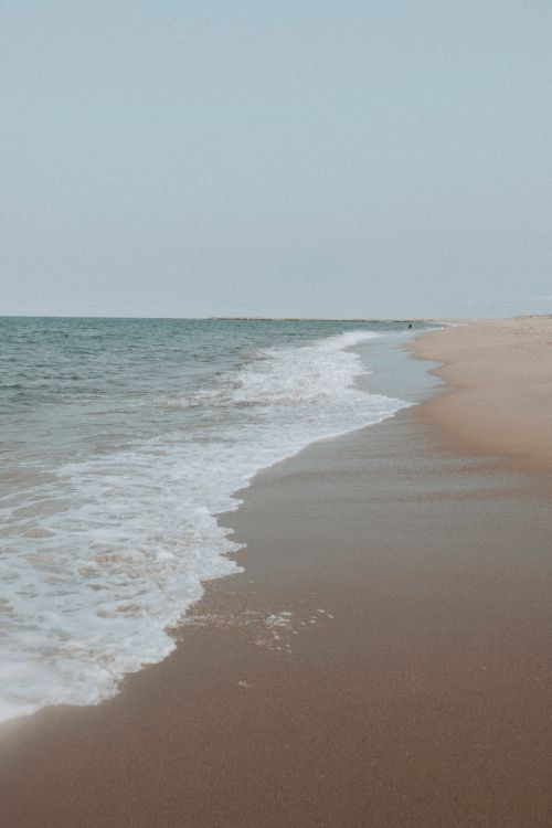 Free A tranquil beach scene with gentle waves washing onto the sandy shore, perfect for travel inspiration. Stock Photo