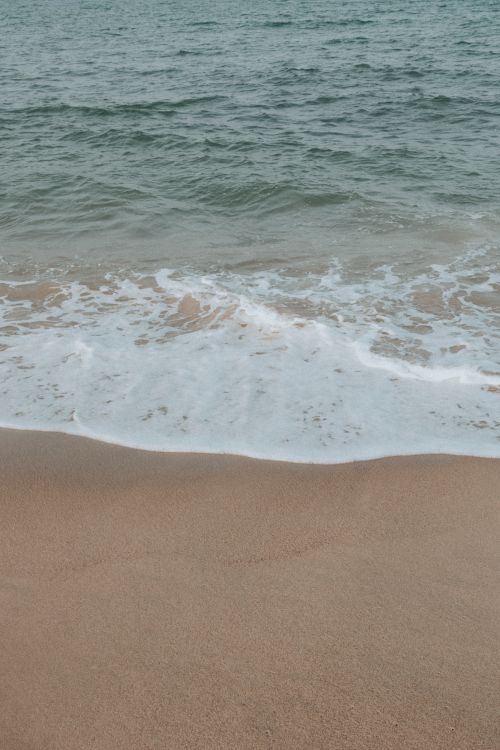 Free Tranquil beach view with gentle waves forming on the sandy shore, perfect for relaxation themes. Stock Photo