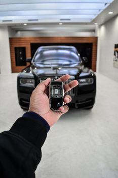 Hand holding a luxury car key with sleek vehicle in background. Perfect for transportation themes.