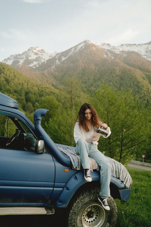 Free Woman sitting on SUV hood in mountain area with outdoor scenery. Stock Photo