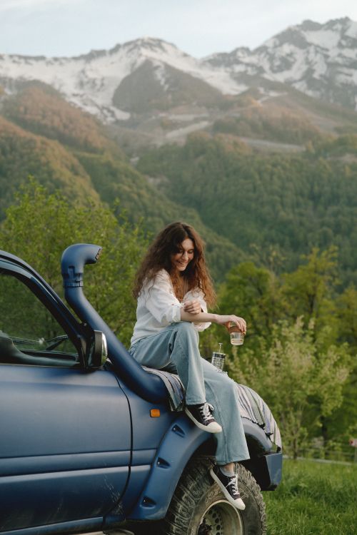 Free Woman sitting on a parked SUV with a breathtaking mountain view in the background. Stock Photo