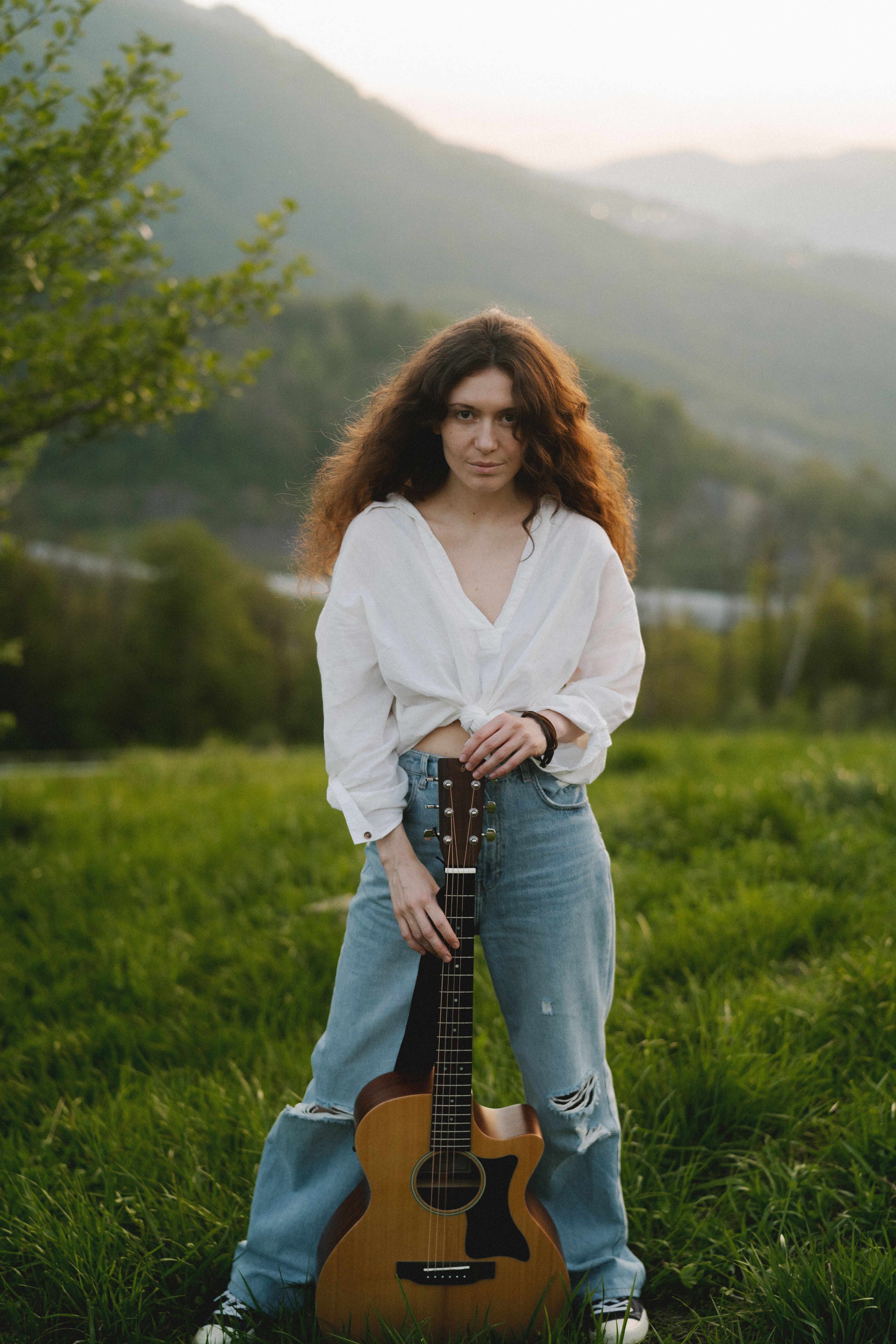 Young woman poses with a guitar in a serene outdoor mountain setting. Perfect for lifestyle and fashion themes.