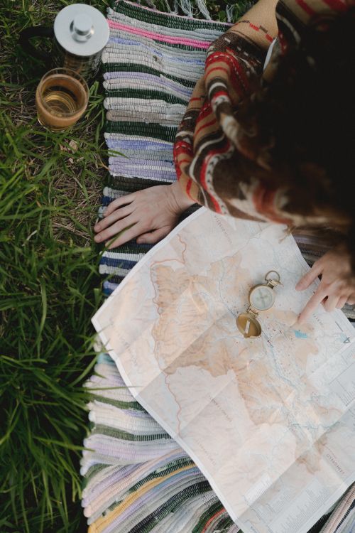 Free Aerial view of a young person planning a hike with a map and compass on a grassy field. Stock Photo