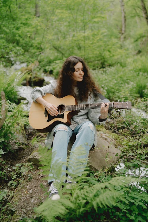 Free Woman Sitting on Rock while Playing an Acoustic Guitar Stock Photo
