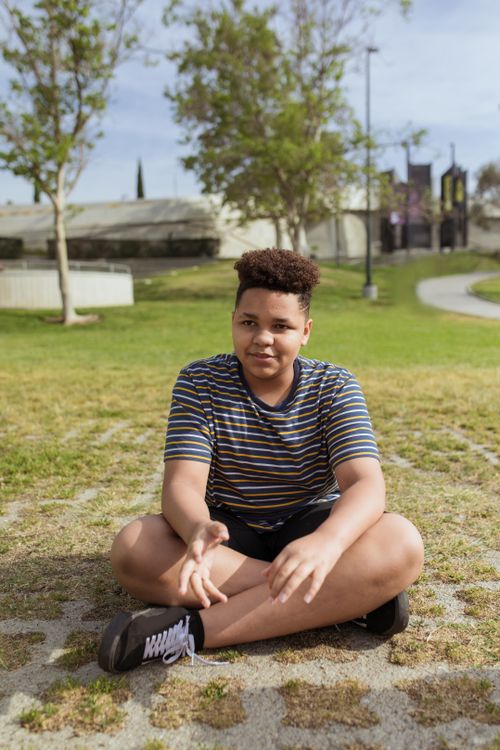 Free Young boy sitting on grass in a sunny park, enjoying a peaceful afternoon. Stock Photo