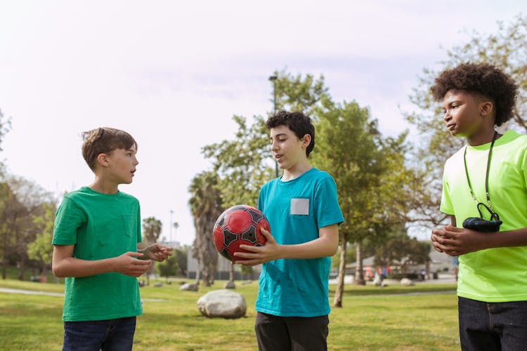 A Boy Holding A Soccer Ball With His Friends At The Park