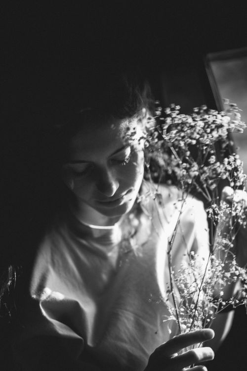 Free Artistic monochrome portrait of a woman tenderly holding delicate flowers in soft lighting. Stock Photo