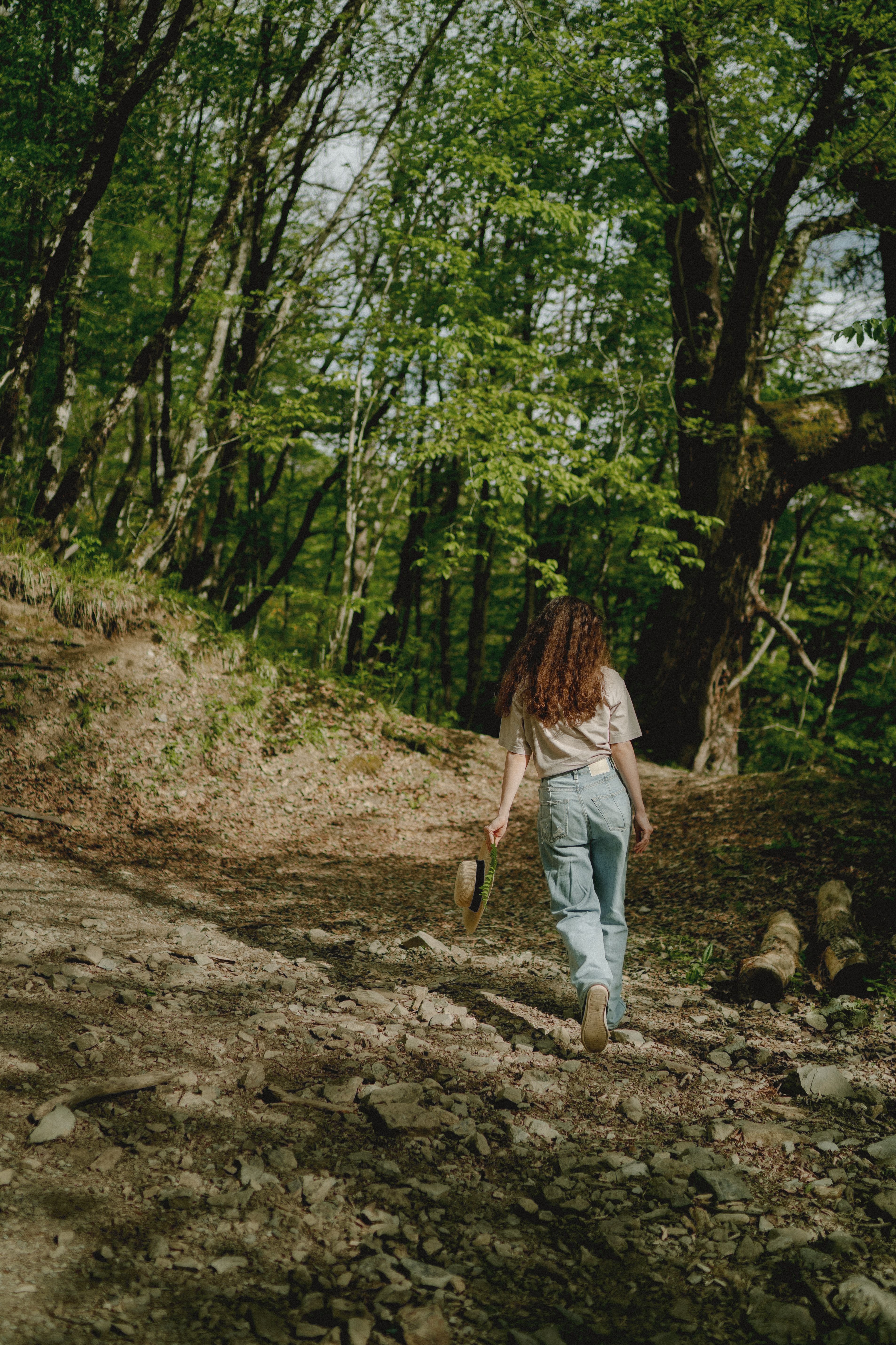 Woman in White Shirt and Denim Pants Walking on Dirt Road in the Forest ...