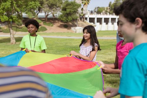 Free Group of kids enjoying a colorful parachute game outdoors in a park during the day. Stock Photo