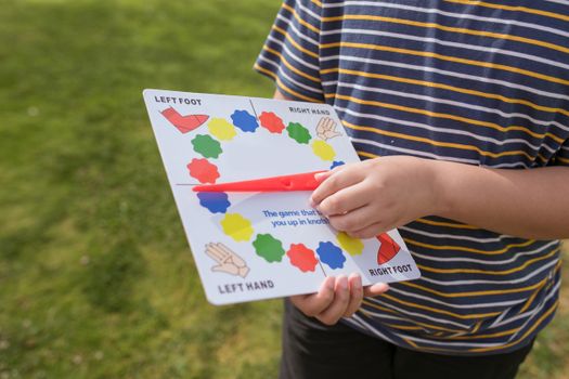 Child holding a Twister game spinner outdoors, ready for play.