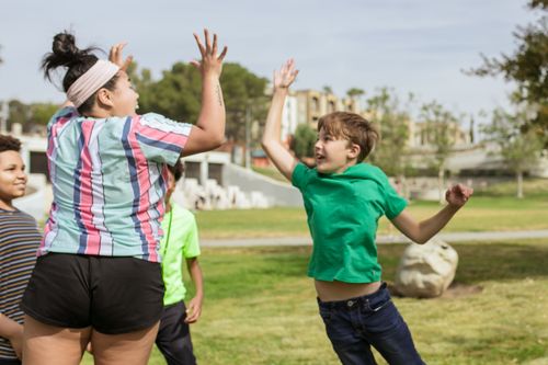 Free Smiling children jumping and high fiving outdoors, enjoying a playful day in a park. Stock Photo