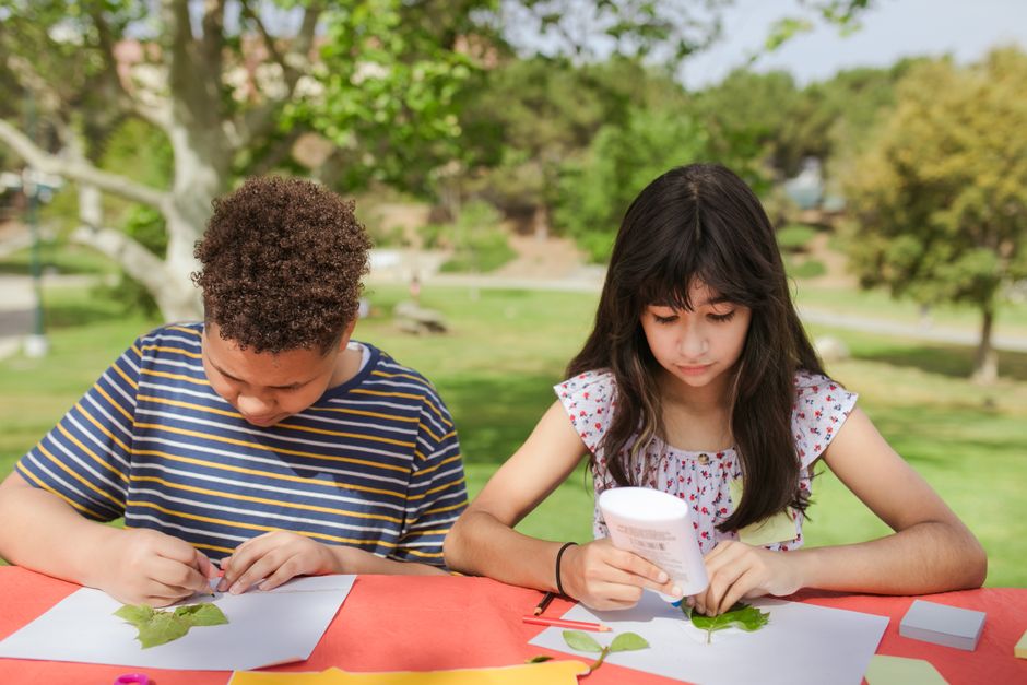 Children participating in arts and crafts activity outdoors with leaves and paper.