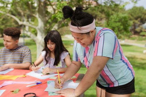 Free Kids engaged in arts and crafts at an outdoor summer camp, drawing creatively on paper. Stock Photo
