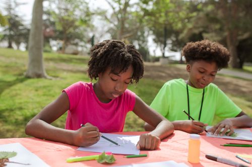 Free Two kids drawing outside on a sunny day, enjoying creative activities with art supplies. Stock Photo