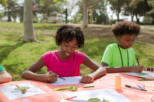 A Young Girl and Boy Writing and Drawing on Papers at the Table