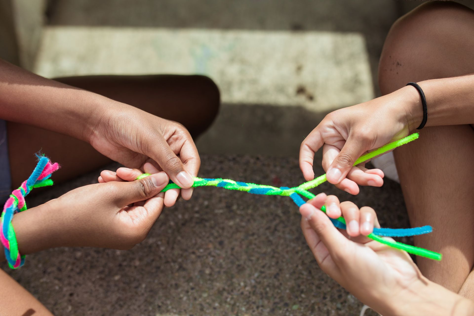 Close-up of kids making vibrant yarn bracelets at summer camp, focusing on hands and creativity.