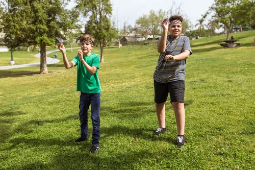 Free Two boys enjoying a sunny day playing with paper airplanes in a green park. Stock Photo