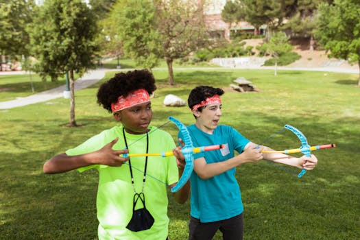Two children practicing archery outdoors, having fun and learning teamwork at summer camp.