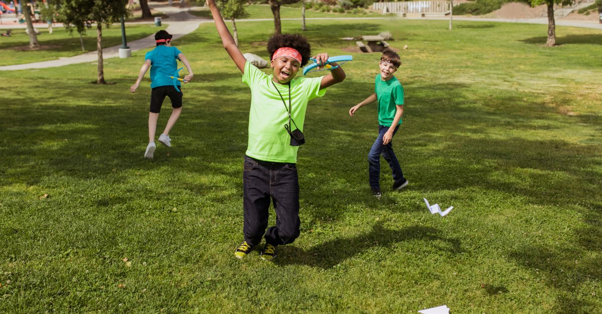 Kids having fun outdoors at summer camp playing with paper airplanes.