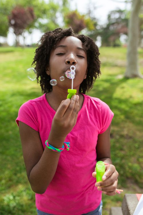 Free Young girl blowing bubbles in a sunny park, enjoying outdoor play. Stock Photo