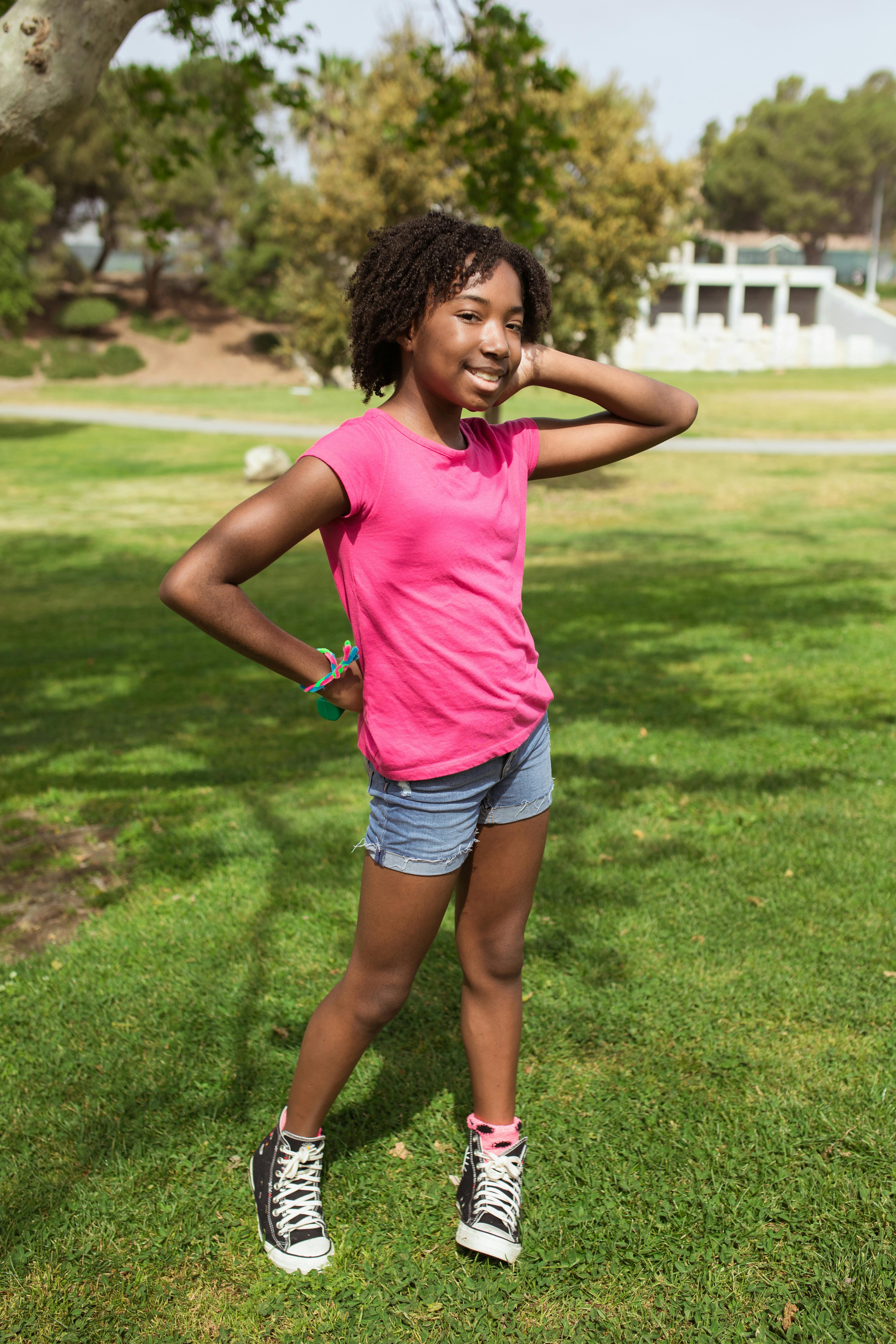 Happy girl in a pink shirt and denim shorts enjoying a sunny day in the park.