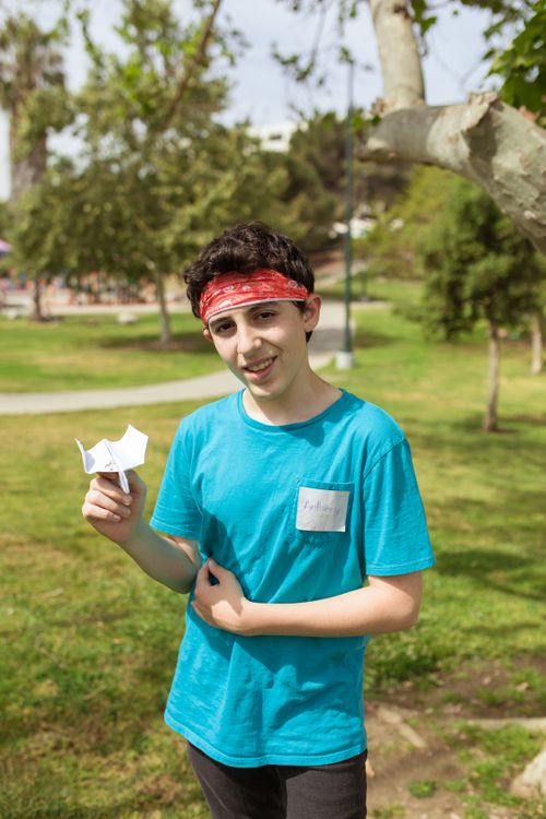 Free Smiling boy holding a paper airplane in a sunny park setting. Stock Photo