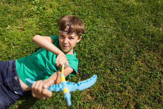 Boy having fun with a toy bow and arrow on the grass in daylight.