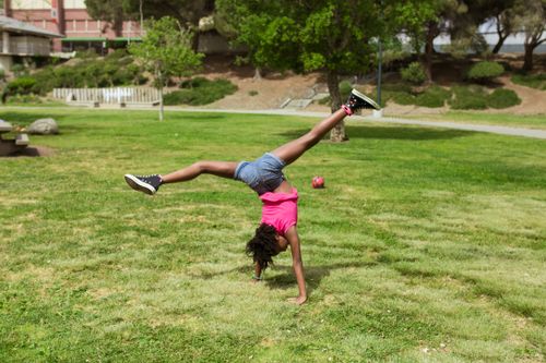 Free A young girl doing a cartwheel on a sunny day in a green public park. Stock Photo