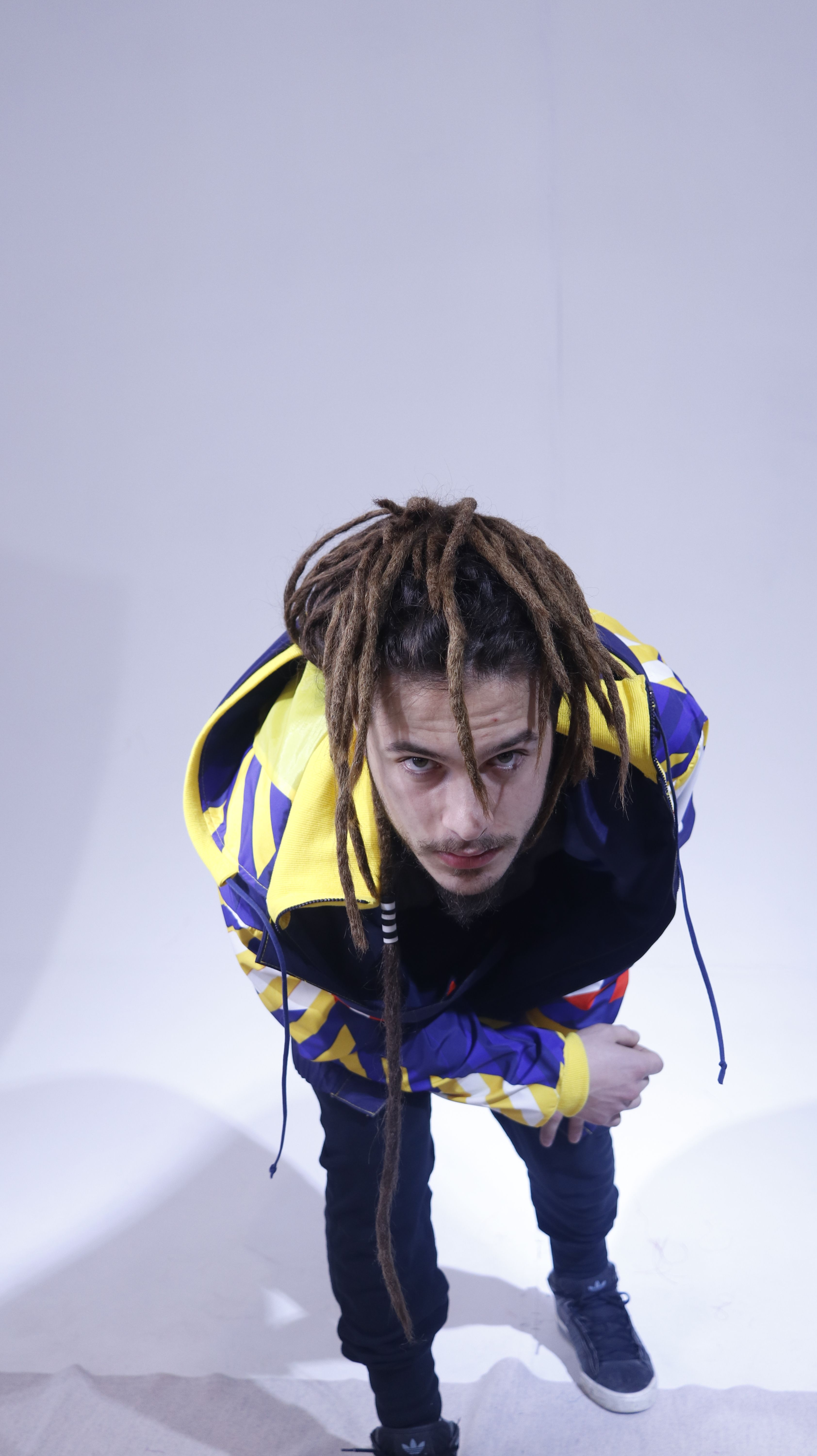 Close-up studio portrait of a man with dreadlocks in a colorful jacket, captured from above.