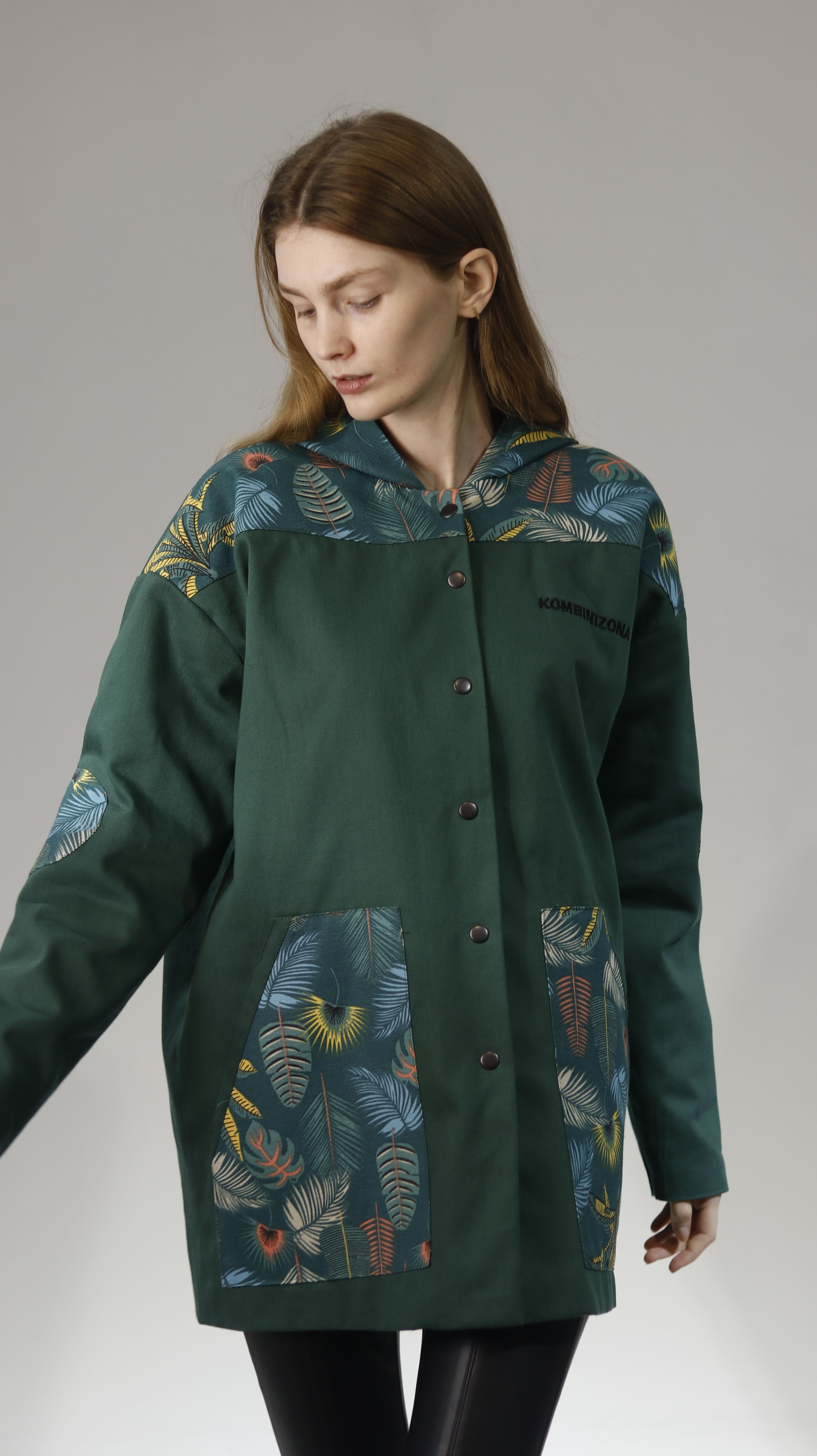 Fashionable woman wearing a green jacket with a unique pattern, looking down in a studio setting.