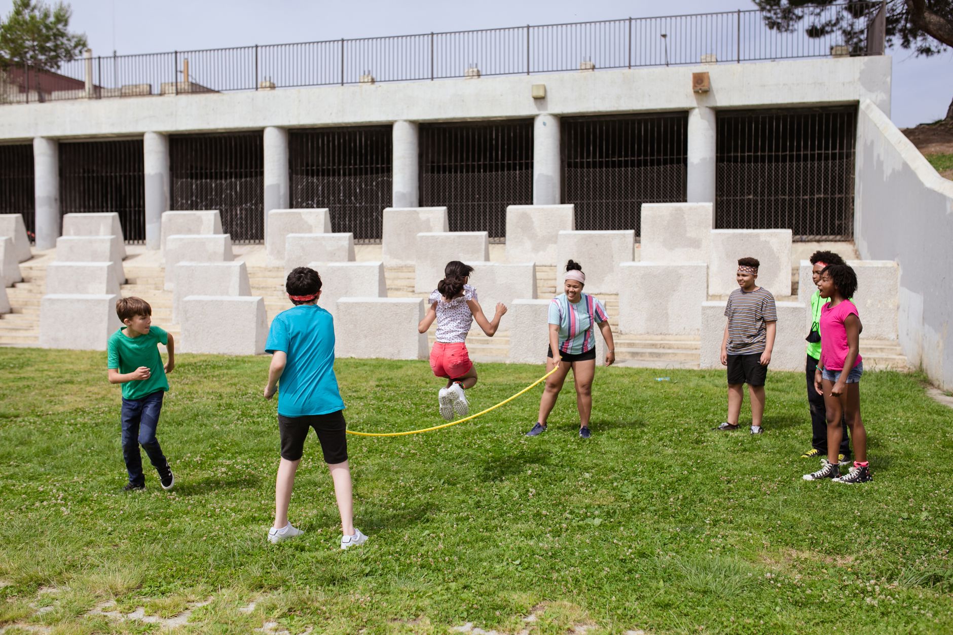 Group of children enjoying a jump rope game outdoors in a sunny park.