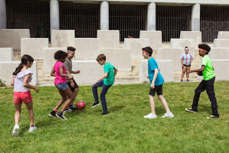 Children Playing Soccer On Green Grass Field