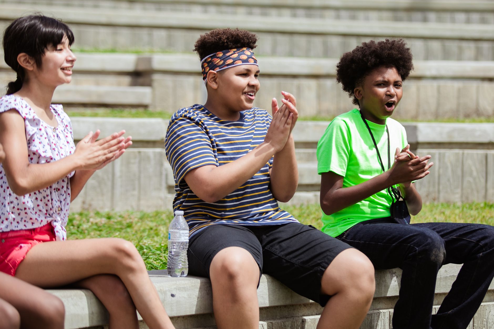 Children of diverse backgrounds clapping hands and cheering on a sunny day outdoors.