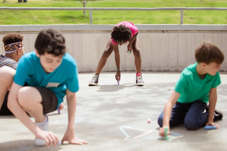 Children Drawing On The Ground Using Chalk 