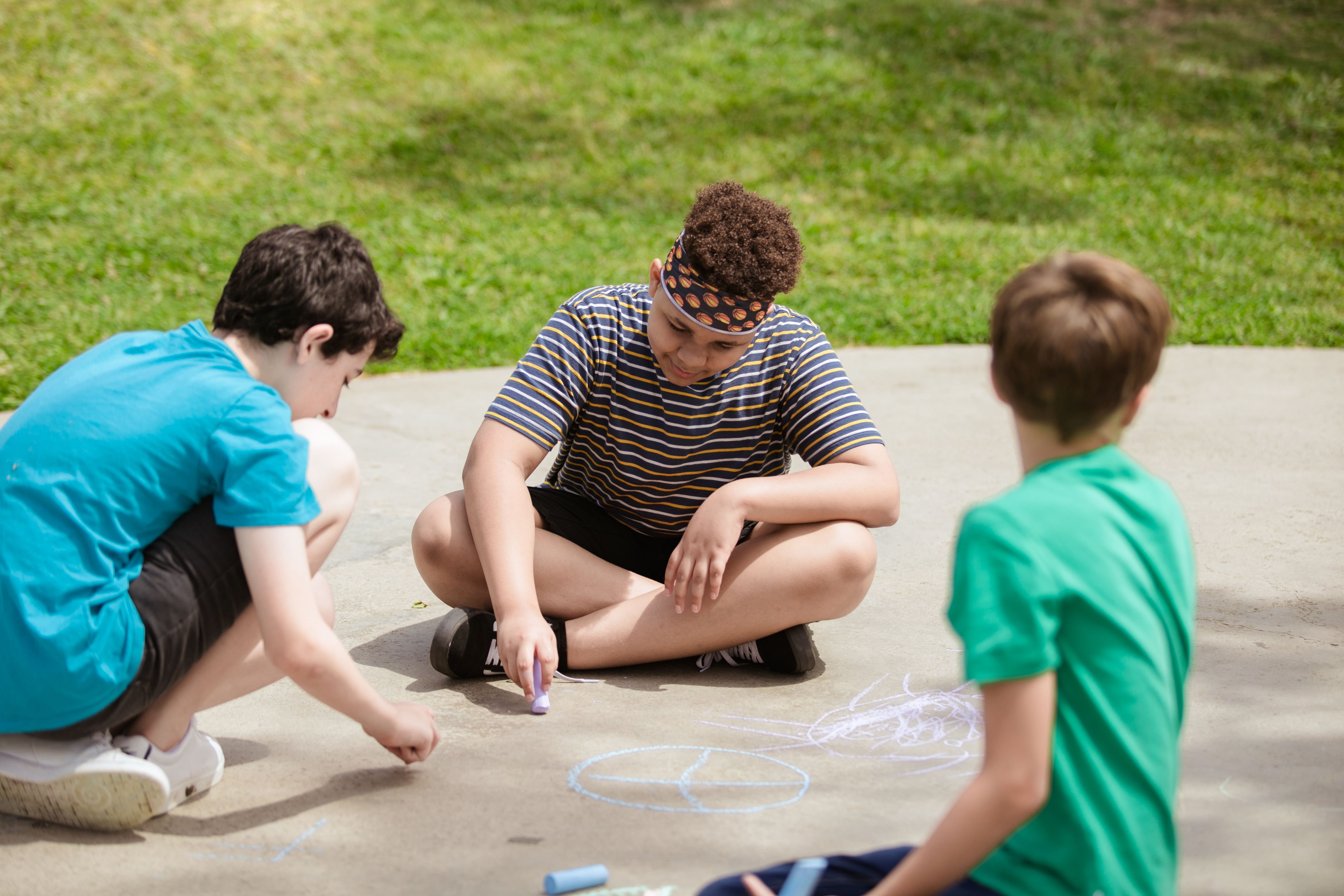 A group of children creatively drawing with chalk on a sunny day at summer camp.
