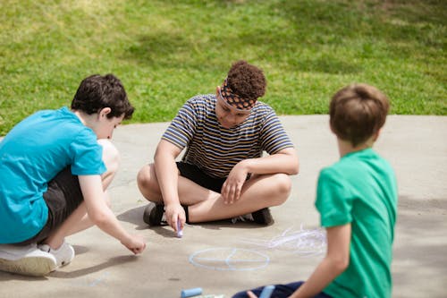 Boys Sitting on the Ground While Drawing Using Chalk 