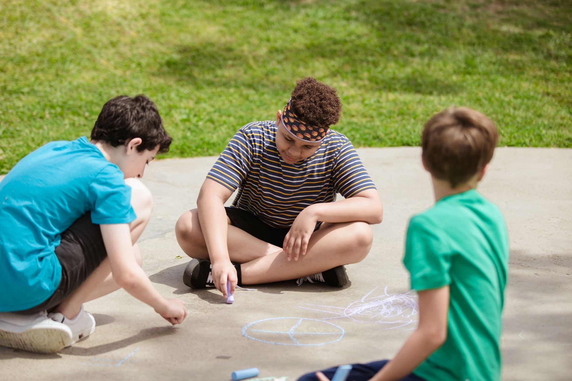 A group of children creatively drawing with chalk on a sunny day at summer camp.