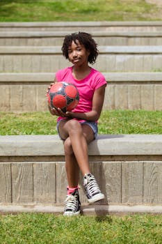 African American girl sitting outside holding soccer ball on a sunny day.