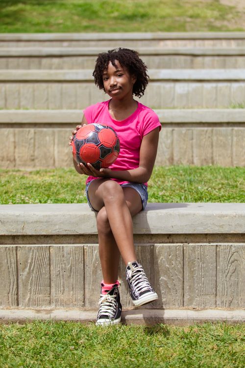 Free African American girl sitting outside holding soccer ball on a sunny day. Stock Photo