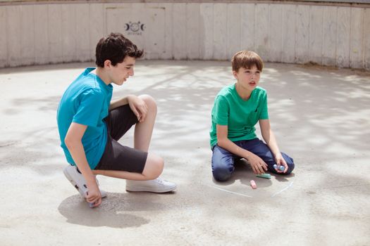 Two boys enjoying drawing with chalk on a sunny day in a park.