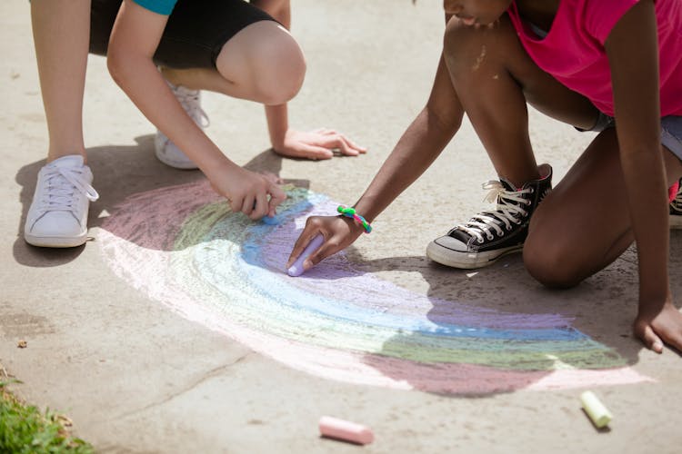 Kids Drawing A Rainbow On The Ground Using Colored Chalks