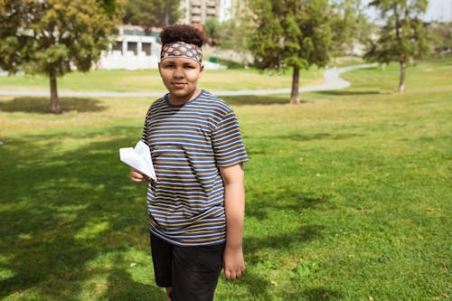 Boy Standing on Grass Holding a Paper Plane