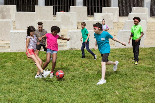 A group of diverse children playing soccer on a grassy field in a casual outdoor setting.