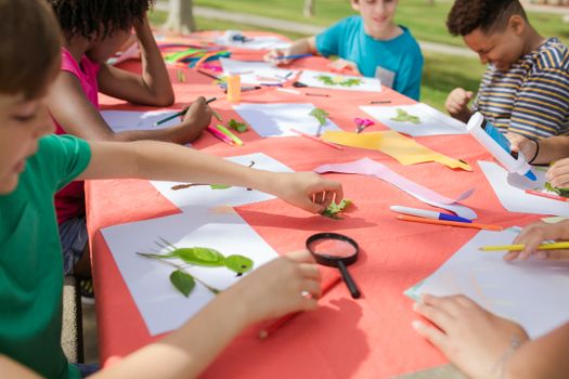Kids engaging in fun arts and crafts, using leaves and paper outside at a colorful table.